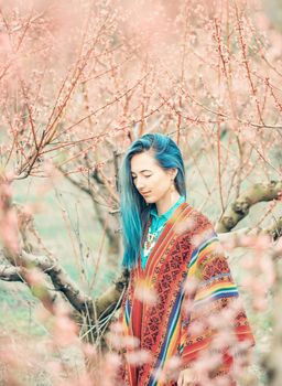 Smiling beautiful young woman boho style walking among blooming cherry-trees in spring.