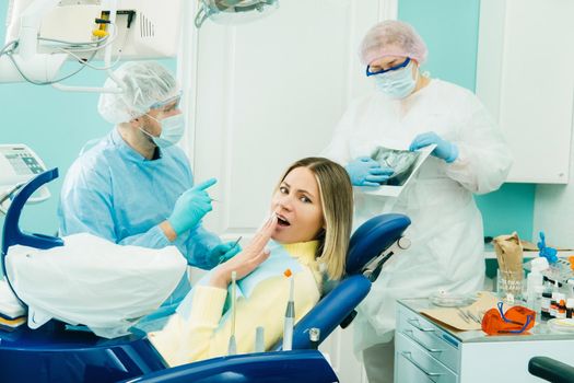 The dentist explains the details of the X-ray to his colleague, the patient is surprised by what is happening.