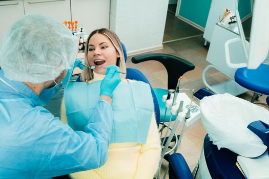 a dentist in a protective mask sits next to him and treats a patient in the dental office.