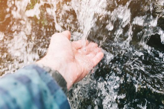Closeup of male hand with water splash of waterfall outdoor.