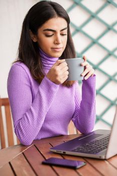 Persian woman sitting in an armchair on her balcony using laptop computer