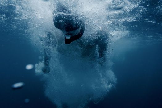 Sporty young man freediver snorkeling underwater surface among many air bubbles.