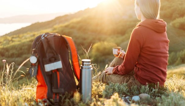 Traveler young woman resting with cup of hot tea in the mountains at sunset.