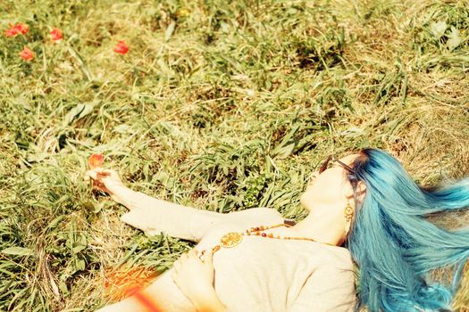 Beautiful young woman with blue hair lying on meadow with red tulips in spring.