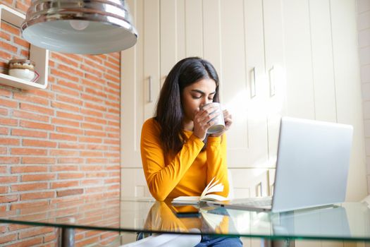 Female architect working at home with a laptop and blueprints. Persian woman. Persian woman with a coffee mug.