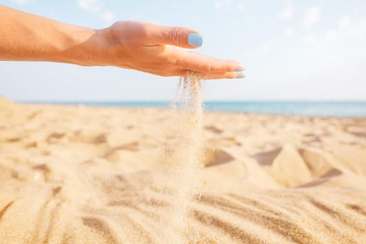 Sand flowing through female hand on beach near the sea.