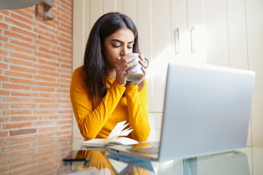 Female architect working at home with a laptop and blueprints. Persian woman. Persian woman with a coffee mug.