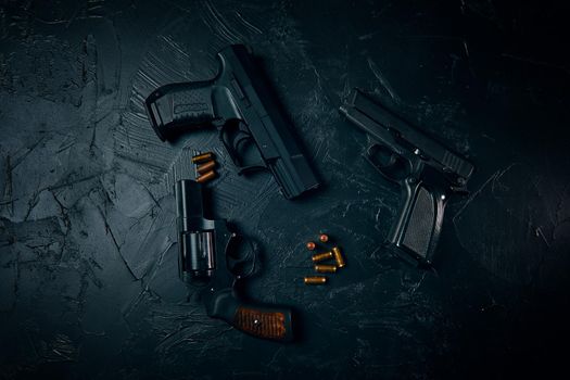 Top view of pistols and gold bullets on black table. Criminal or police arsenal. Dangerous firearms. Vintage revolver with a drum. 9mm hand gun.