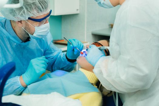 A young beautiful girl in dental glasses treats her teeth at the dentist with ultraviolet light. filling of teeth.