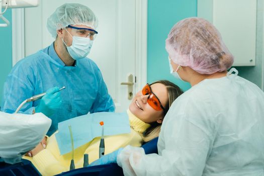 The patient smiles in the dentist's chair in a protective mask and instrument before treatment in the dental office.