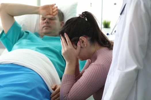 Girl crying near man lying on bed in ward clinic. Monitoring all vital functions patient. Medicine use modern and proven practice diagnostic and treatment methods. Preoperative preparation