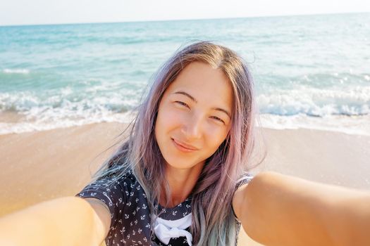 Smiling young woman taking selfie on background of sea on summer vacations, point of view.
