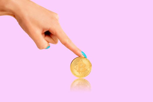 Female hand pointing to cryptocurrency bitcoin on a pink background.