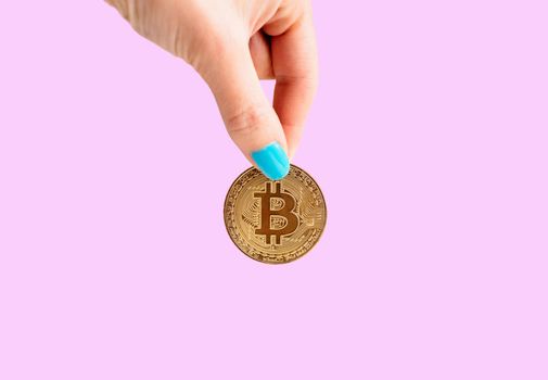 Woman’s hand with gold coin bitcoin on a pink background, symbol of virtual money.