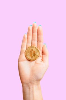 One gold bitcoin on female palm hand on a pink background, symbol of crypto currency.