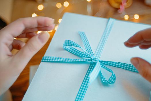 Close-up of women's hands and blue checkered ribbon on white gift box. Christmas or Birthday surprise.