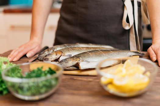 Unrecognizable woman will cook fish trout, hands on kitchen wooden table near the ingredients of dish.