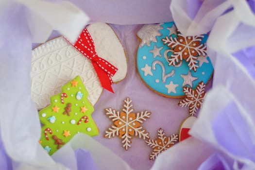 Christmas gift box with gingerbread inside. Cookies with icing in form of mittens, New Year trees and snowflakes. White and lilac parchment paper for wrapping sweets.