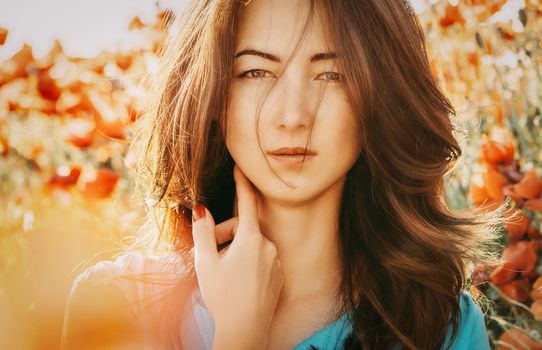 Portrait of beautiful brunette young woman on background of poppies flowers, looking at camera.