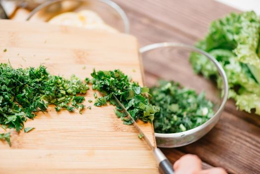 Unrecognizable woman pours sliced greenery from board into a plate for dish in the kitchen, view of hand close-up.