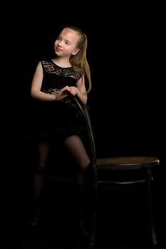 Portrait of a little girl who stands near an old Vienna chair on a black background. Studio photo on the cover of the magazine.