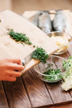 Woman’s hands pours sliced greenery from board into a plate in the kitchen.