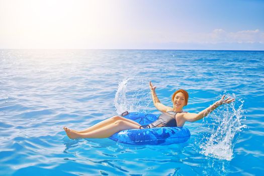 Red-haired girl splashes water. Beautiful young woman resting on an inflatable ring in the sea water. Summer holidays. Cheerful woman with a swimming balloon.
