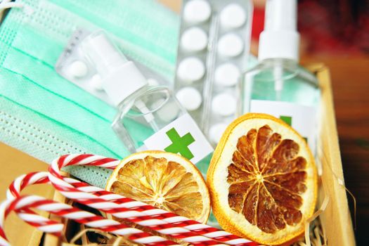 Gift box with antiseptics, pills, lollipops, medical masks and dried oranges. New Year's Eve during pandemic. Holidays in quarantine. Christmas surprise.