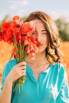Portrait of beautiful brunette young woman with bouquet of red poppies outdoor.