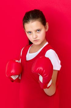 Teenage girl posing in boxing gloves. Portrait of sportive boxer girl dressed sportswear ready to fight. Child training on red background. Healthy lifestyle, sport and fitness concept