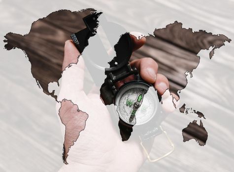 Double exposure of travel compass in a hand with map of world on a wooden background.