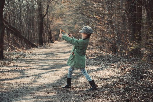 little girl playing with a slingshot in the woods, photo in vintage style