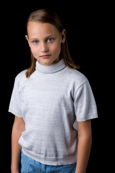 Portrait of pretty blonde preteen girl. Stylish girl dressed gray jumper posing against black background and looking seriously at camera. Close up shot of beautiful child