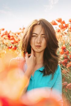 Portrait of beautiful brunette young woman in red poppies meadow, looking at camera.
