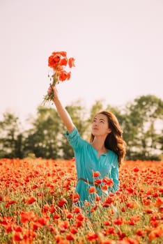 Smiling beautiful brunette young woman holding bouquet of red poppies over her head in flower meadow.