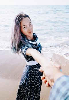 Couple in love resting on beach summer vacations. Young woman holding man's hand and leading him on coast, point of view.