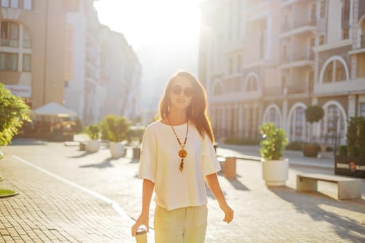 Beautiful young woman summer casual style walking in city street with cup of coffee.