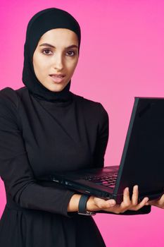 muslim woman in hijab with laptop technology learning pink background. High quality photo