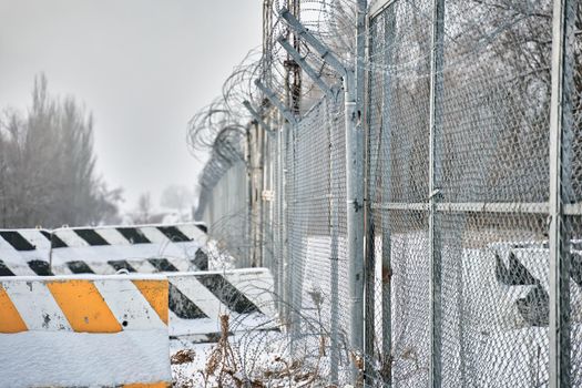 Concrete road blocks on ground. Barbed wire fence on border in winter. Closing for quarantine. Private object near highway. Maximum security detention facility. Unauthorized entry is prohibited.