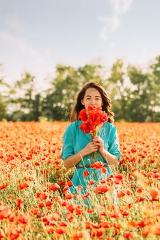 Beautiful young woman standing with bouquet of red poppies in meadow on summer day.