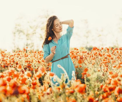 Attractive brunette young woman walking in poppies meadow in summer.