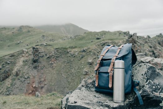 Backpack and thermos on stone in the mountains outdoor, concept of wanderlust.