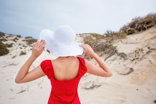 beautiful young woman in evening red dress and white hat on a background of a sand desert