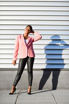 Black woman, model of fashion, standing on urban wall. African american female wearing suit with pink jacket with sunset light.