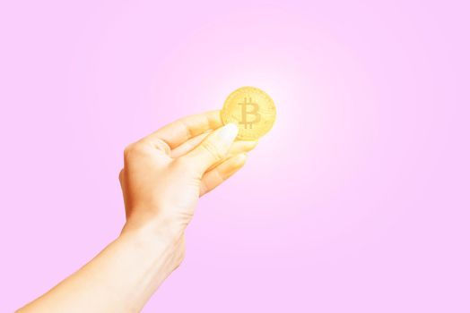 Hand holding symbol of cryptocurrency - gold bitcoin on a pink background.