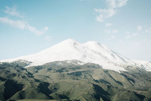 Mount Elbrus with snowy peaks and green fields on sunny day, Caucasus mountain range, Russia.
