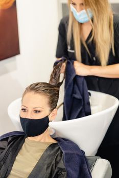 Female hairdresser washing a client's head in a salon, protected by a mask against Covid-19