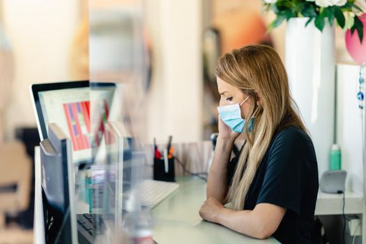 Female hairdresser answering the phone to give her clients an appointment, wearing a protective mask, at a hairdresser's. Business and beauty concepts