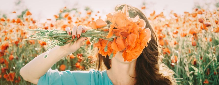 Unrecognizable young woman covered her face with bouquet of red poppies flowers in summer outdoor.
