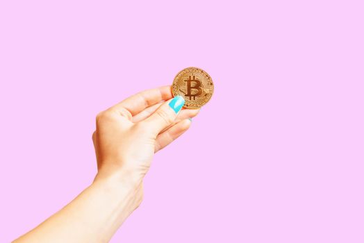 Hand holding symbol of virtual money - gold bitcoin on a pink background.